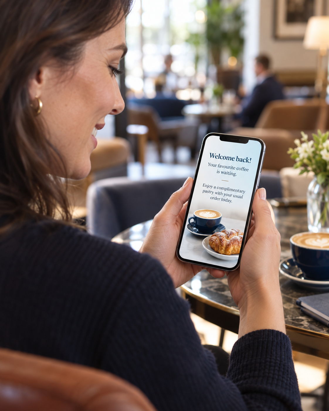 Customer in a hotel café receiving a personalised welcome-back coffee offer on her phone.